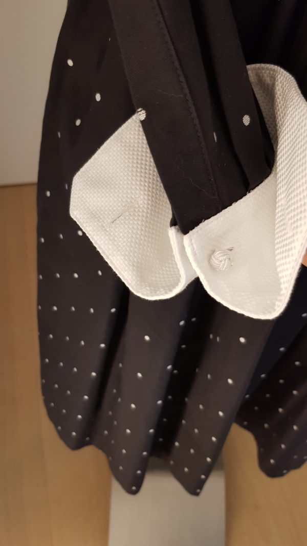 Raffinierts Smokingkleid mit leicht ausgestelltem Rock, mit versteifter Smokingbrust in Piqué, weißen Knöpfen, weißem Mascherl in Piqué, weiße Manschetten mit Manschettenknöpfen, schwarzer Baumwollstoff mit kleinen weißen Tupfen, seitlicher Zippverschluss, breiter Bund