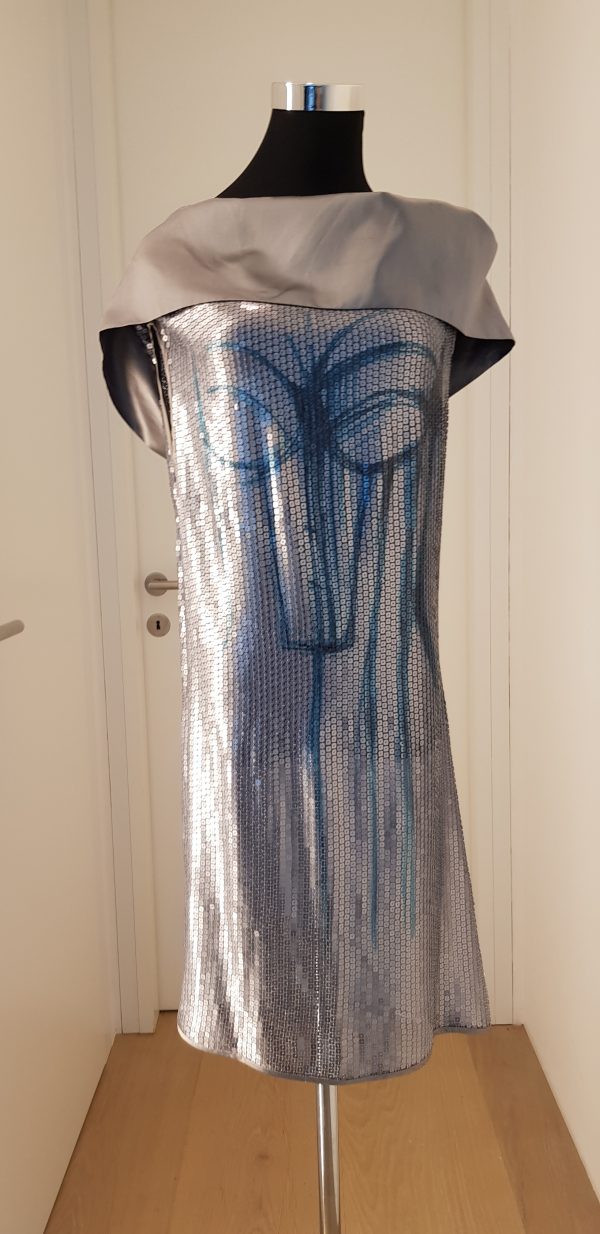 Silbernes Paillettenkleid mit extrem breitem silbernen Schalkragen, blaues Ornament vorne