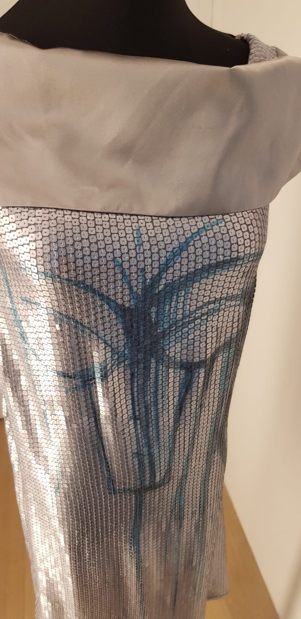 Silbernes Paillettenkleid mit extrem breitem silbernen Schalkragen, blaues Ornament vorne