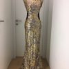 Langes Paillettenkleid in gold mit leichter Schleppe, Rücken und Taillie frei, über Schulterblätter verläuft Schließe, Lederriemen sorgen für Taillenanpassung